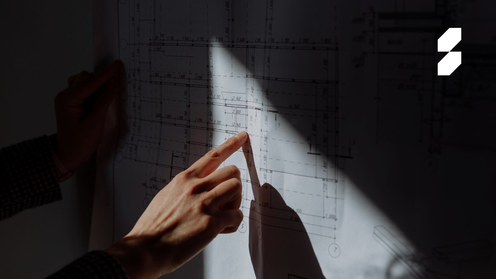Ruka ukazuje na architektonický pôdorys v páse svetla